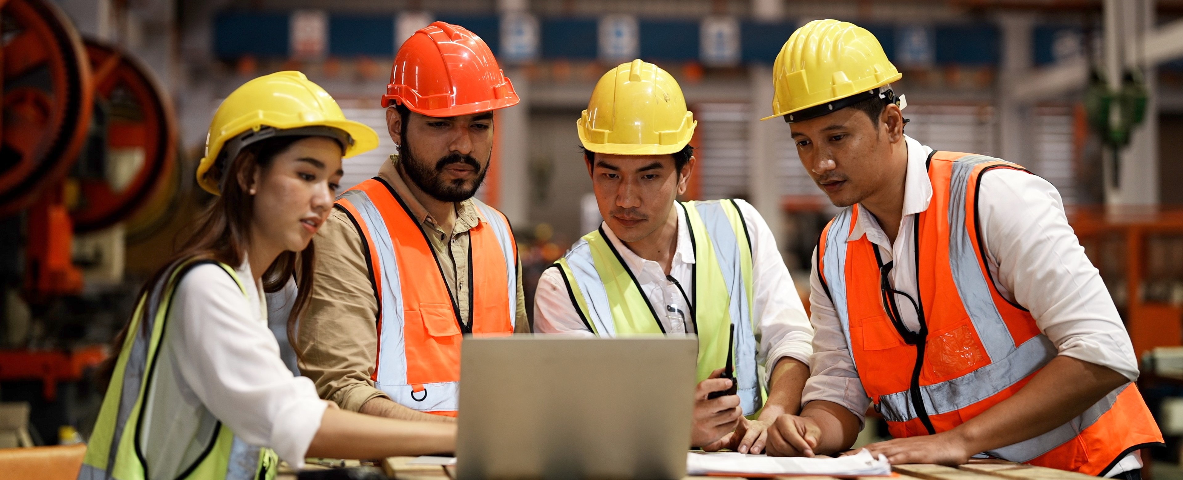 Group of individuals in hard hats and vests surrounding a laptop