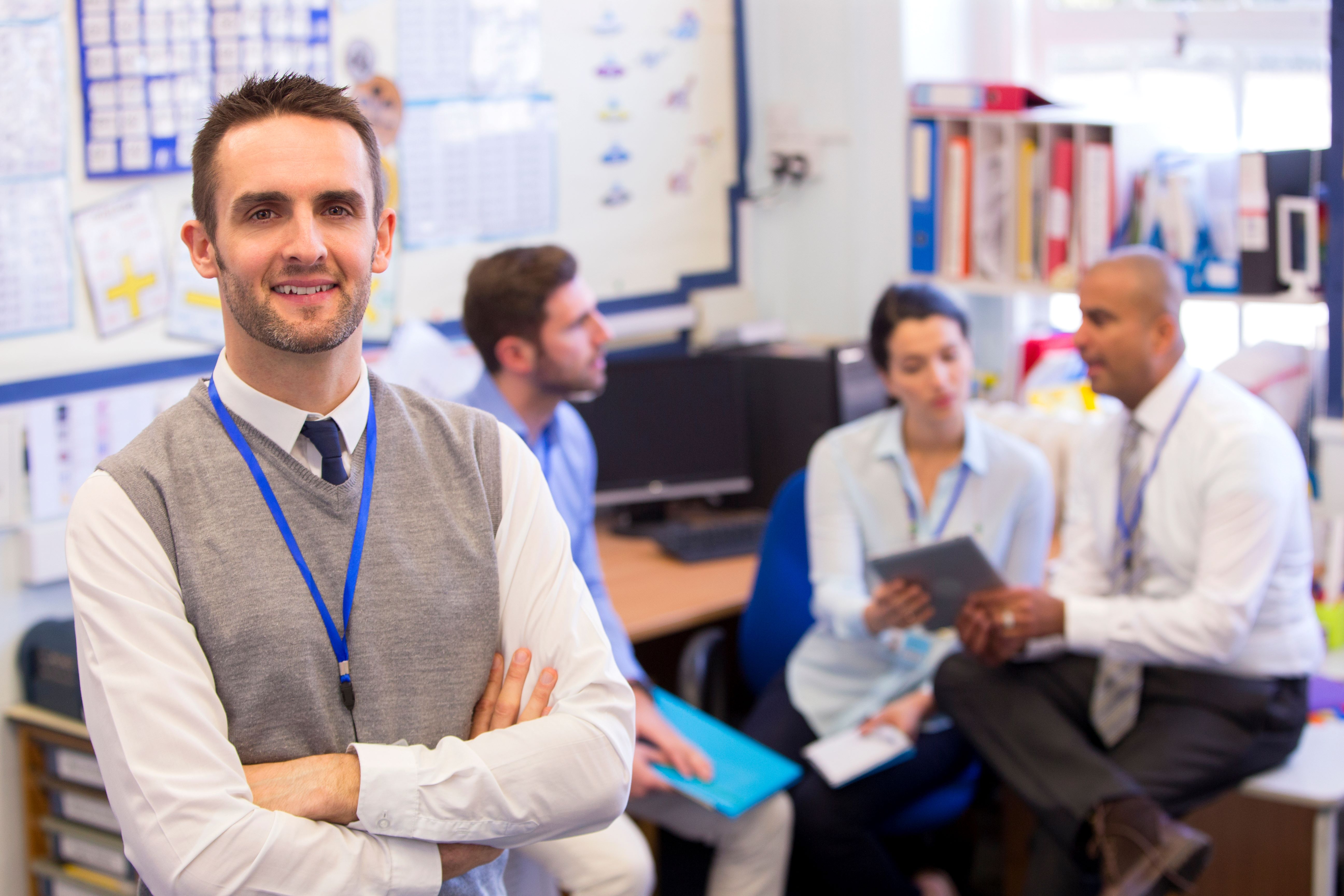 Male school administrator in a classroom with other administrators talking in the background.